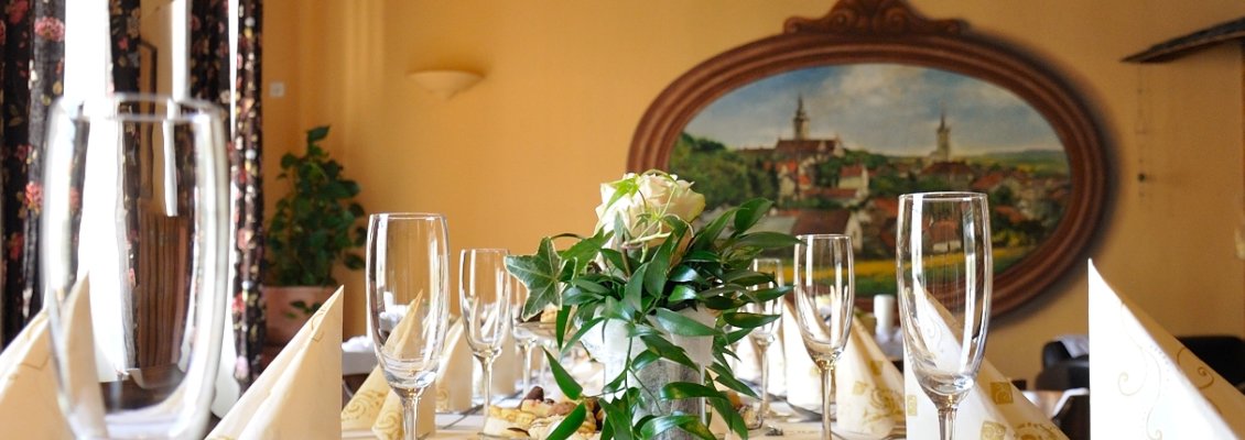 Krémová svatební tabule s kyticí. V pozadí nástěnná malba Pacova.